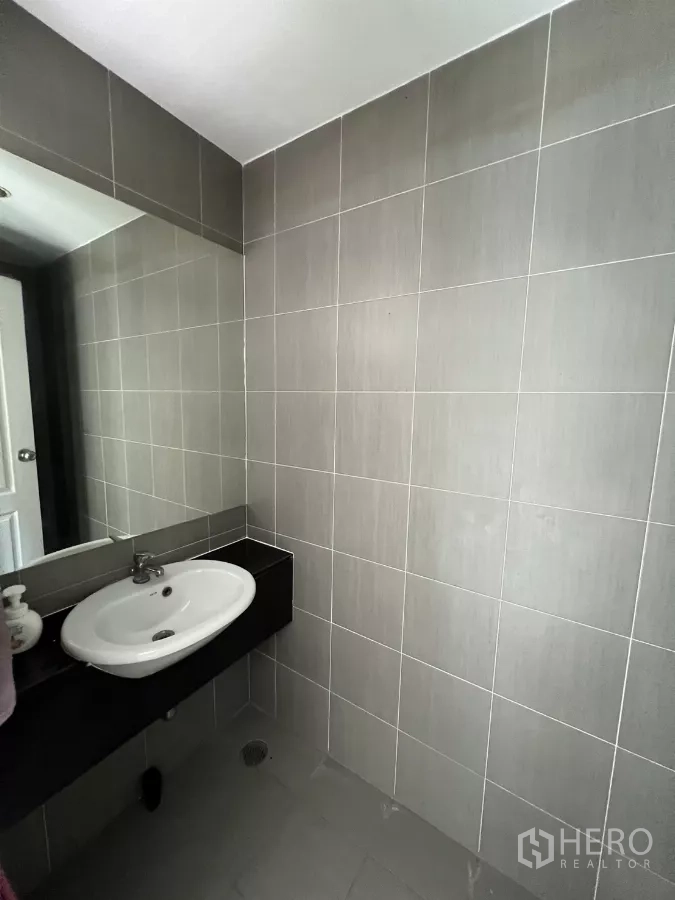 Townhouse for rent in Suan Luang, Bangkok - Guest bathroom with gray tiled walls, vanity, and mirror.