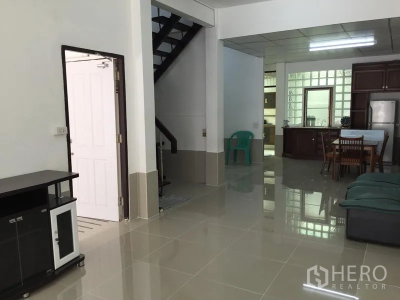 Townhouse for rent in Phra Khanong, Bangkok - Open-plan living and dining area with glossy tile floors and staircase to upper level.