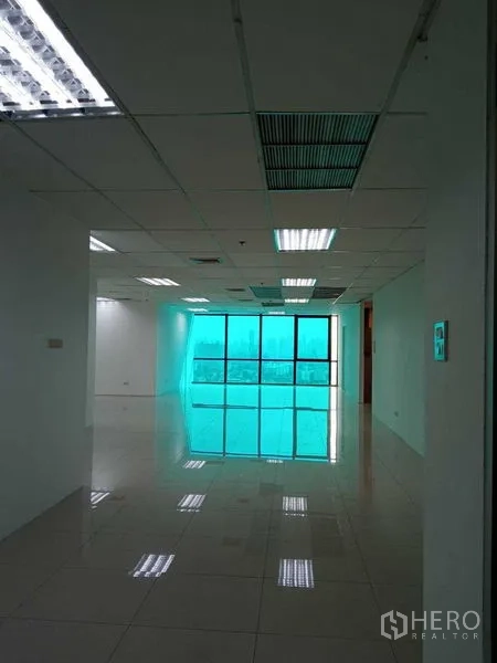 办公空间 出租在Huai Khwang, Bangkok - 开放式办公室，亮面瓷砖地面、吊顶照明与整面着色落地窗，可眺望曼谷城市景观。