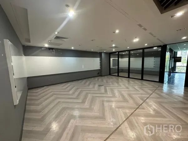 Office Space for rent - Open-plan office with herringbone floors, a long wall whiteboard, recessed lighting and glass partitions.