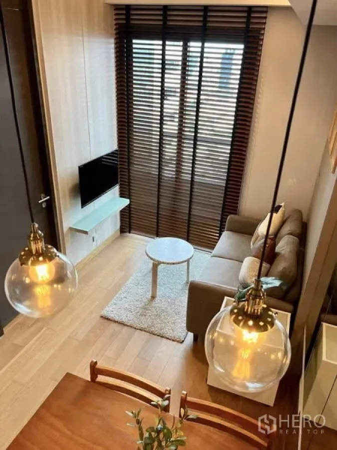 Condominium for rent or sale - Overhead view of living and dining space with pendant lights, TV and tall window blinds.