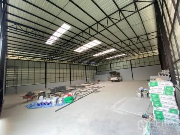 Warehouse for rent in Saphan Sung, Bangkok - Wide open storage hall with metal frame roof, skylight panels and stacks of construction supplies.