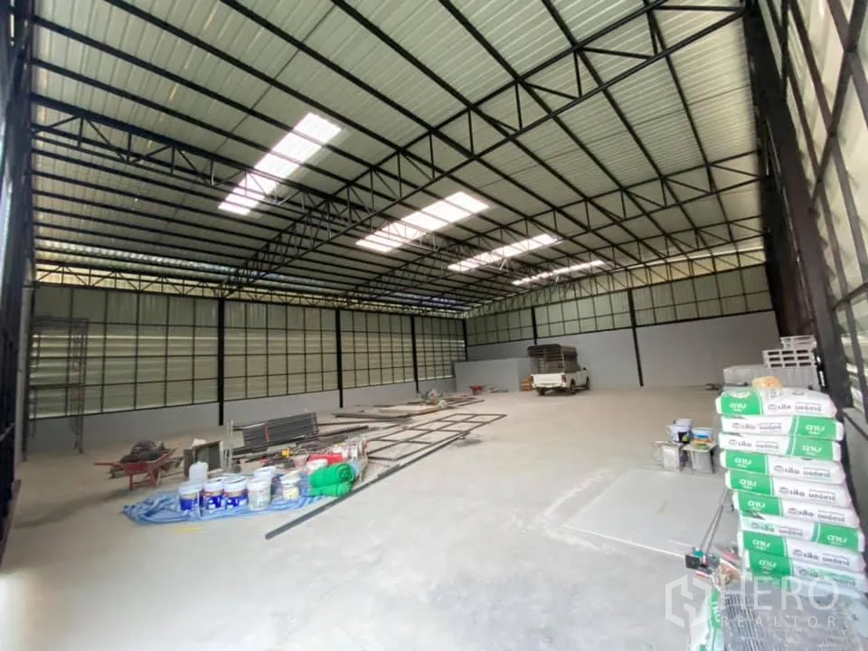 Warehouse for rent in Saphan Sung, Bangkok - Wide open storage hall with metal frame roof, skylight panels and stacks of construction supplies.