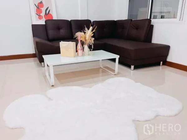 联排别墅 出租在Huai Khwang, Bangkok - 温馨客厅，棕色L形沙发、玻璃茶几与白色绒毛地毯。