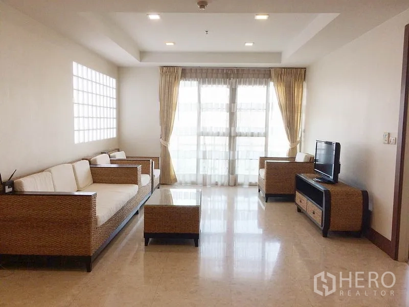 Condominium for rent in Khlong Toei, Bangkok - Bright living room with rattan sofa set, TV console and floor-to-ceiling windows.