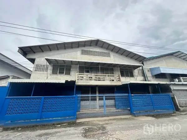 Factory for rent in Lam Luk Ka, Pathum Thani - Two-storey factory facade with blue gates and metal awnings in Lam Luk Ka.