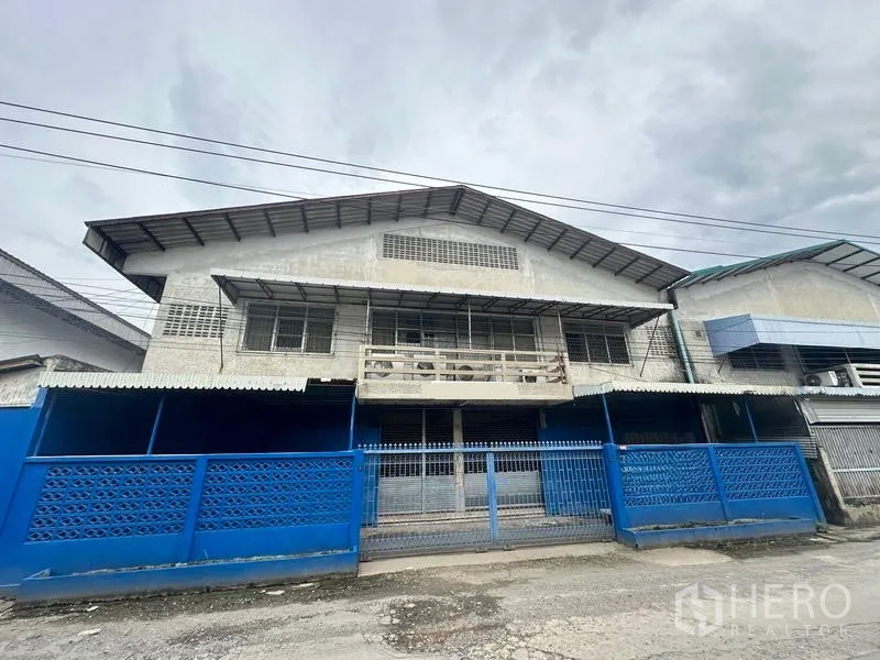 Factory for rent in Lam Luk Ka, Pathum Thani - Two-storey factory facade with blue gates and metal awnings in Lam Luk Ka.