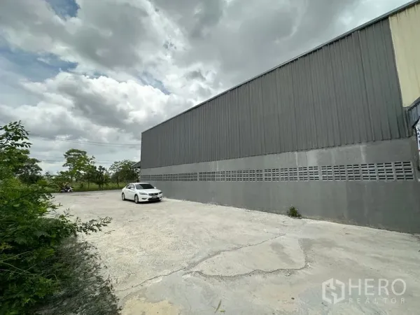 Warehouse for rent in Thanyaburi, Pathum Thani - Side view of the warehouse showing a long concrete yard and greenery along the boundary.