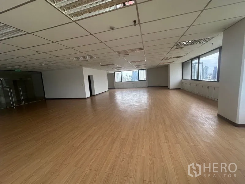 办公空间 出租在Bang Rak, Bangkok - 空置办公楼层，转角大窗与日光充足，荧光灯照明，玻璃门入口。