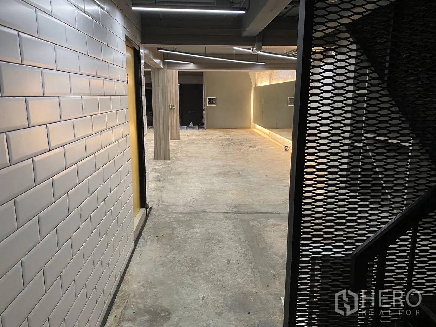 Retail Space for rent in Phaya Thai, Bangkok - Corridor with white subway tiles and a metal-mesh staircase opening to the main open-plan retail area.