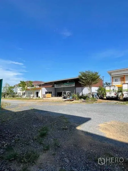 Warehouse for rent or sale in Pathum Thani - Wide yard view of a modern warehouse with covered loading bay and gravel driveway.