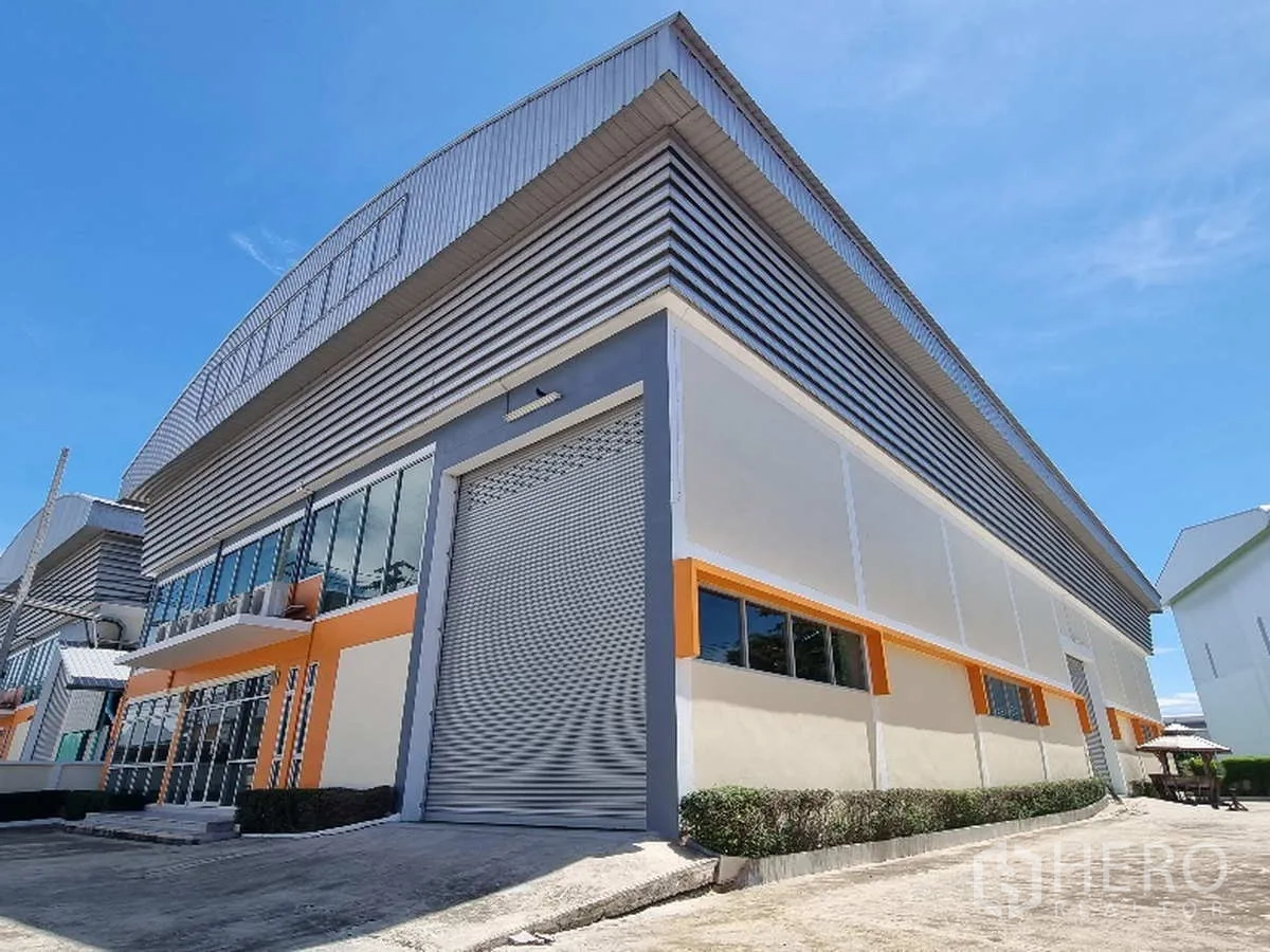 Factory for rent in Samut Prakan - Corner view of the warehouse facade with insulated metal cladding and loading door.