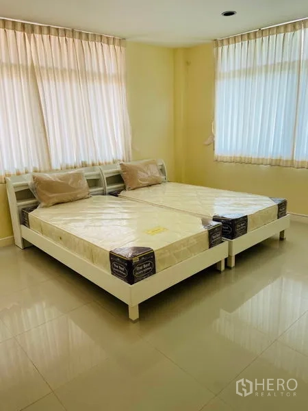 Detached House for rent in Watthana, Bangkok - Corner bedroom with two single beds, wraparound windows and sheer curtains.