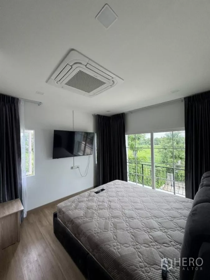 Detached House for rent in Thanyaburi, Pathum Thani - Primary bedroom with balcony view, large windows and wall-mounted TV.