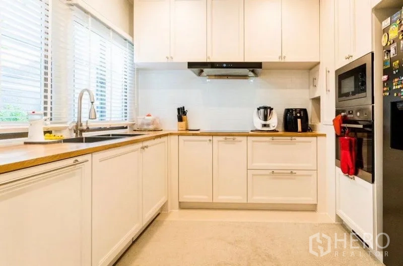 Detached House for rent - U-shaped kitchen with white cabinetry, wood countertops, sink by the windows, and built-in appliances.