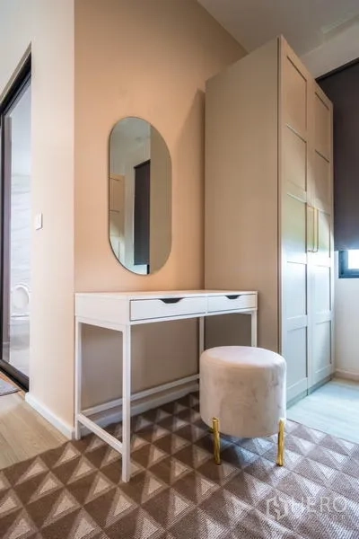 Townhouse for rent or sale in Suan Luang, Bangkok - Vanity corner with mirror, upholstered stool, and tall wardrobe near the bathroom.