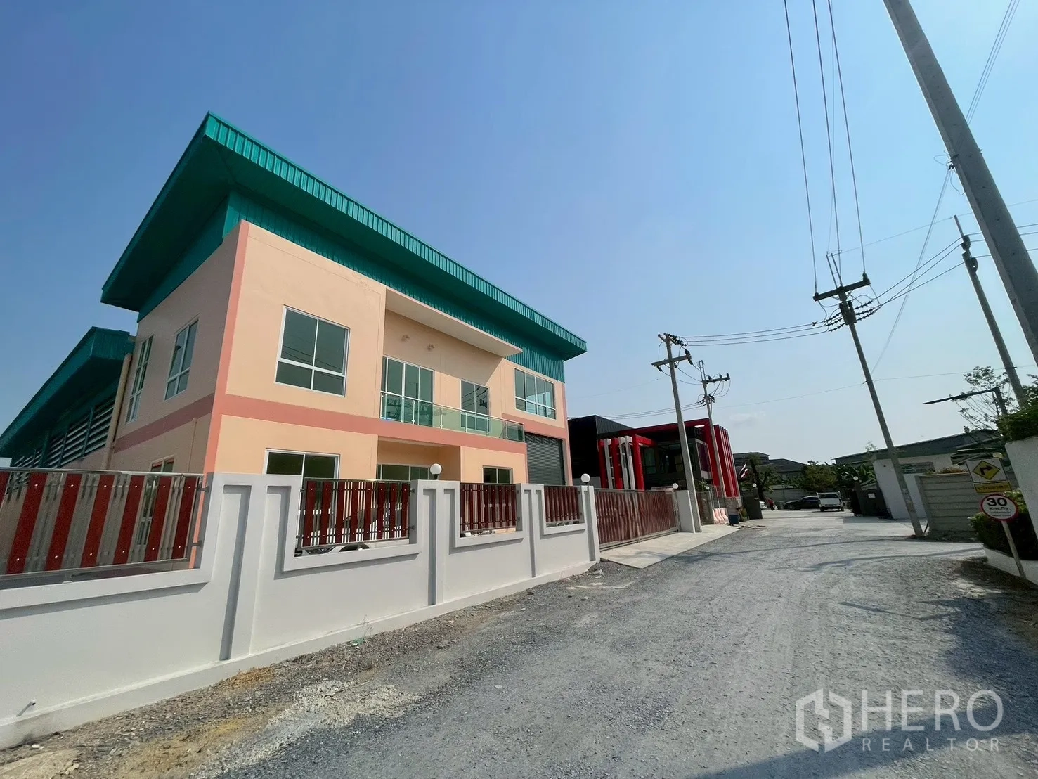Factory for sale in Sam Phran, Nakhon Pathom - Street view of the factory building with perimeter wall and green roof eaves.