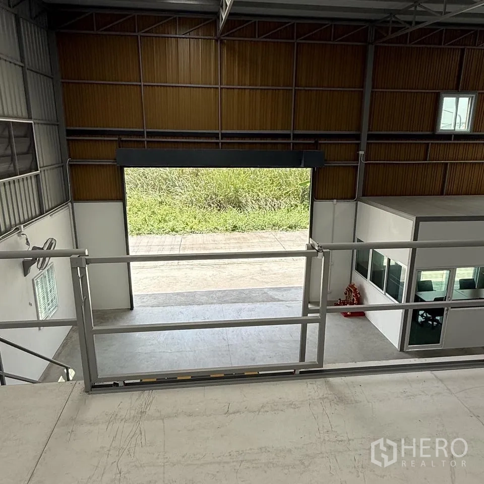 Warehouse for rent or sale in Khlong Luang, Pathum Thani - View from the mezzanine toward a large roller shutter and ground-floor office unit.