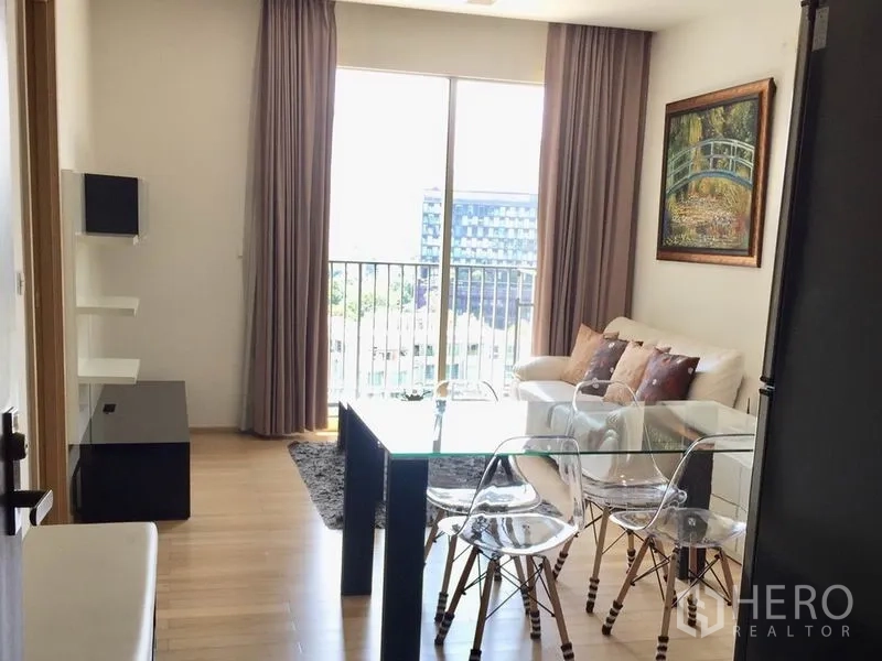 Condominium for rent in Khlong Toei, Bangkok - Bright living and dining area with glass table, wood floors, and balcony city view.