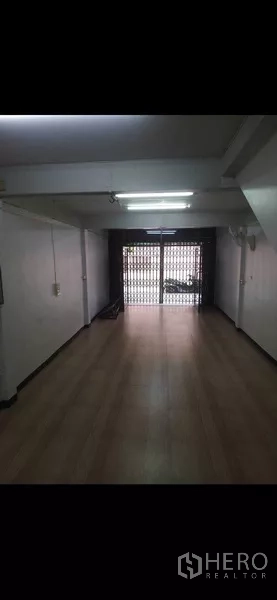 Shophouse for rent or sale in Phra Khanong, Bangkok - Long shop interior facing the metal folding gate with bright fluorescent lighting.
