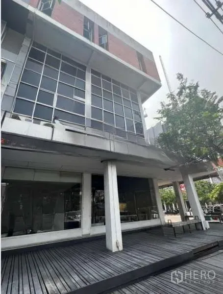 Shophouse for rent or sale in Khlong Toei, Bangkok - Angled exterior of a multi-storey shophouse featuring a raised wooden deck and large grid windows.
