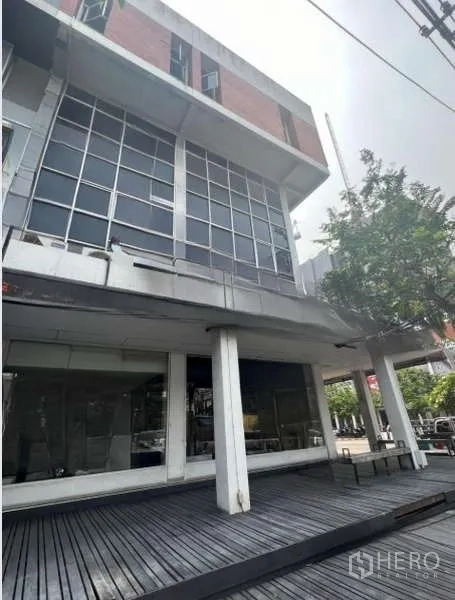 Shophouse for rent or sale in Khlong Toei, Bangkok - Angled exterior of a multi-storey shophouse featuring a raised wooden deck and large grid windows.