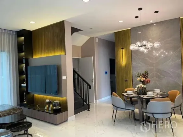 Detached House for rent in Bang Phli, Samut Prakan - Open‑plan living and dining room with TV feature wall, marble floor and modern chandelier beside the staircase.