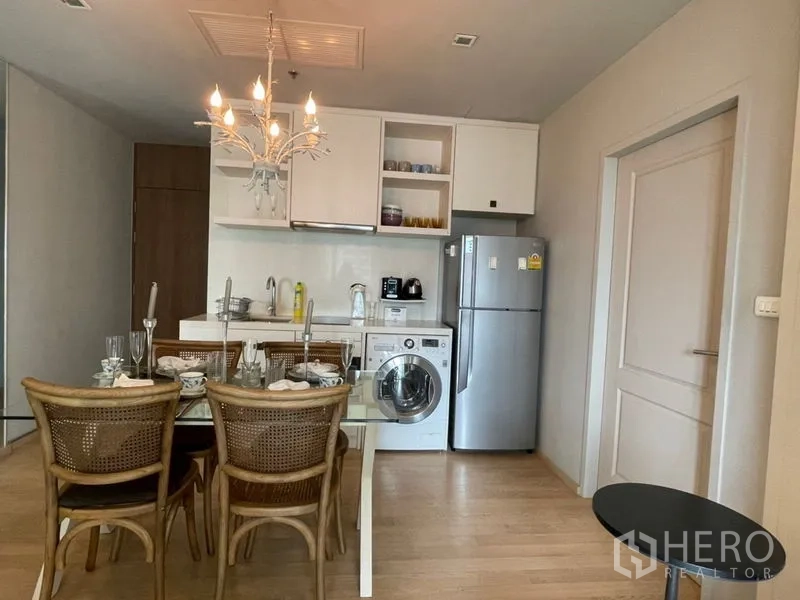 Condominium for rent in Bangkok - Kitchen and dining area with chandelier and glass table on light wood flooring.