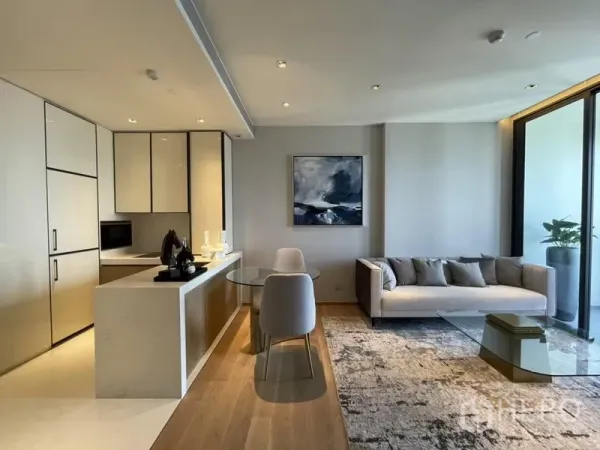 Condominium for rent in Khlong Toei, Bangkok - Open-plan kitchen with stone island, glass dining table, and bright living room leading to a balcony.