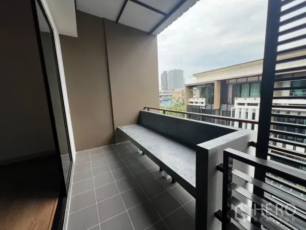 Townhouse for rent or sale in Khlong Toei, Bangkok - Private balcony with roof cover and built‑in bench overlooking neighboring modern townhomes and city skyline.