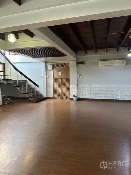 Detached House for rent in Watthana, Bangkok - Spacious living area with wood-look flooring, exposed beams and an open staircase.