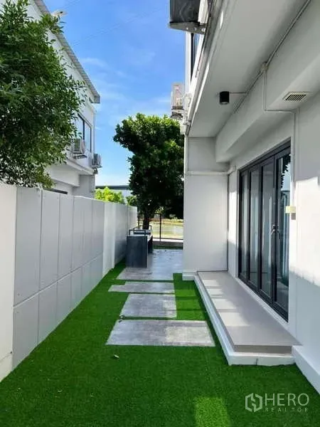 Detached House for rent or sale in Bang Phli, Samut Prakan - Narrow side yard featuring artificial grass, stepping stones and a high privacy wall.