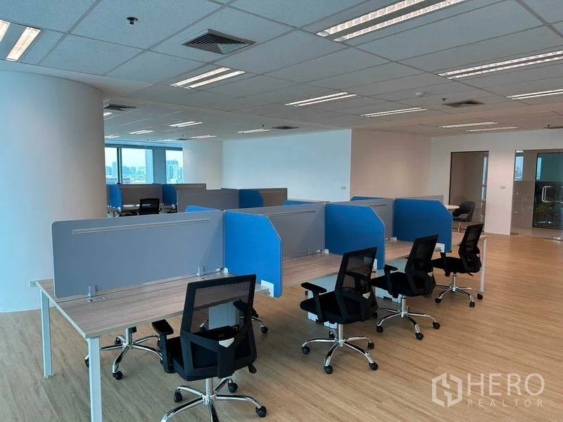 Office Space for rent - Cluster of cubicles with swivel chairs in a bright corner office with a glass meeting room beyond.