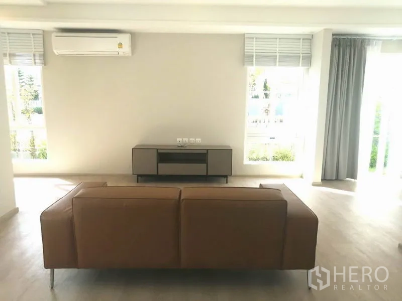 联排别墅 出租在Prawet, Bangkok - 采光充足的客厅，浅木地板、皮沙发、电视柜与空调。