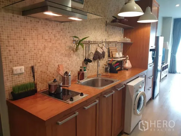 Condominium for rent or sale in Bangkok - Modern galley kitchen with mosaic backsplash, cooktop, sink and washing machine.