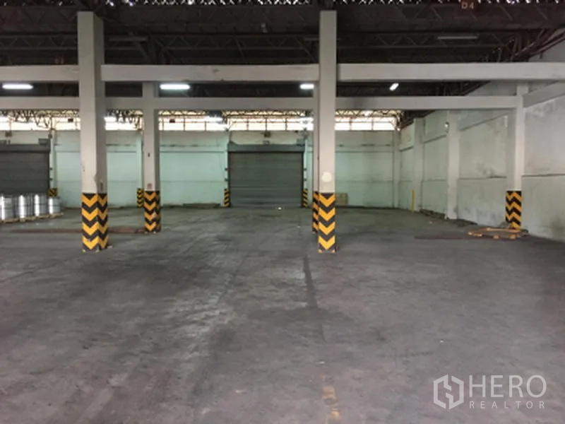 Warehouse for rent in Pathum Thani - Empty warehouse facing multiple roll-up shutter doors and loading area with marked columns.