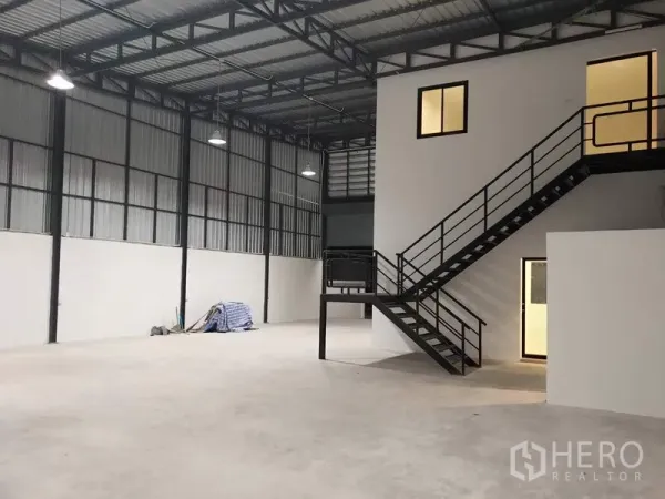 Factory for rent in Lam Luk Ka, Pathum Thani - Warehouse interior with high steel roof, mezzanine office and black metal staircase.