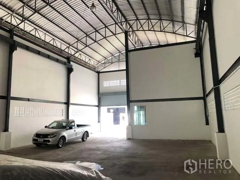 Warehouse for rent in Pak Kret, Nonthaburi - Spacious warehouse interior facing the front roller door with steel beams and concrete floor.