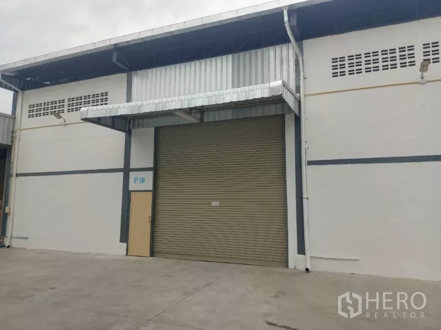 Warehouse for rent in Suan Luang, Bangkok - Warehouse exterior with large roller shutter door, metal awning, and wide driveway in the On Nut area of Bangkok.