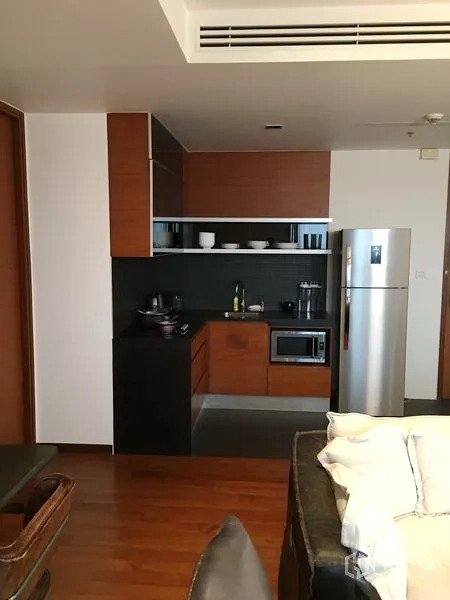 Condominium for rent or sale in Khlong Toei, Bangkok - Open-plan kitchen with wood cabinets, black backsplash, microwave and stainless refrigerator.