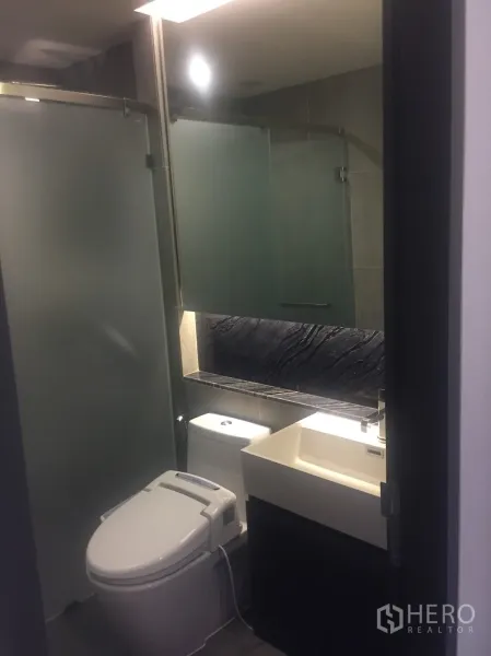 Condominium for rent in Khlong Toei, Bangkok - Contemporary bathroom with frosted glass shower, vanity, and bidet toilet.