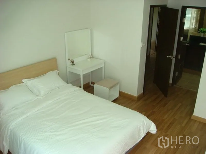 Apartment for rent in Khlong Toei, Bangkok - Cozy bedroom with bed and vanity table, doorway to an ensuite bathroom.