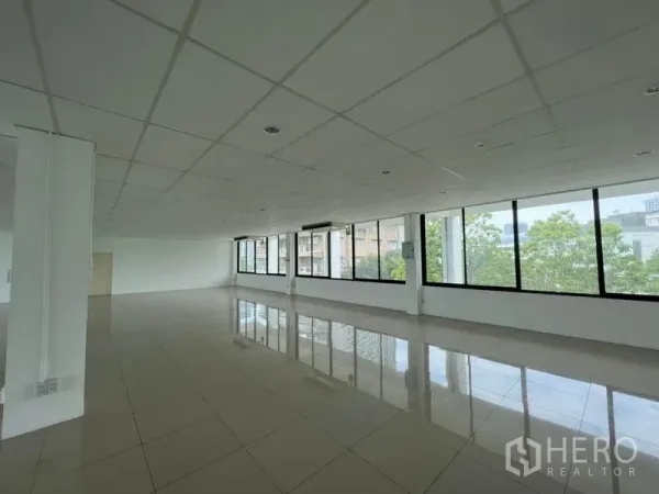 Office Space for rent - Spacious empty office with large black-framed windows, glossy tiles and city and tree views providing abundant natural light.