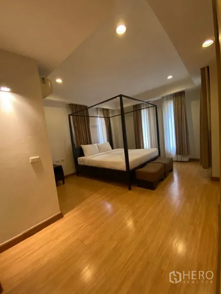 Condominium for rent in Watthana, Bangkok - Primary bedroom with a four-poster bed, bench seating, wood flooring, and corner windows.
