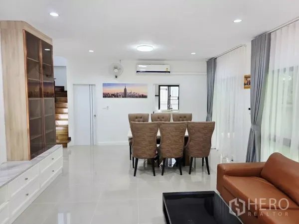 Detached House for rent in Prawet, Bangkok - Open-plan living and dining area with eight-seat table, sofa, staircase and wide windows.