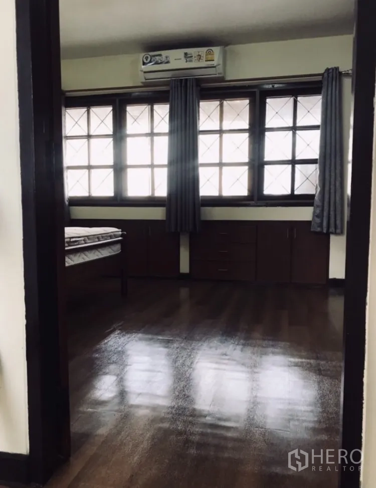 Townhouse for rent in Watthana, Bangkok - Upstairs bedroom with large grid windows, curtains, built-in cabinets and wood floors.