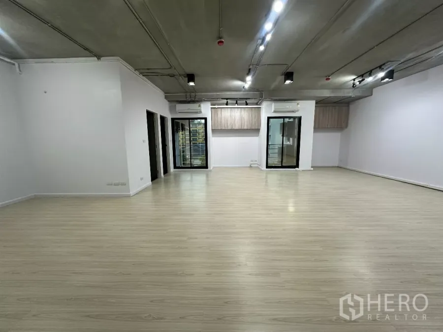 Office Space for rent in Watthana, Bangkok - Wide office hall with spotlight tracks, two glass entry doors, light timber floors and white walls.