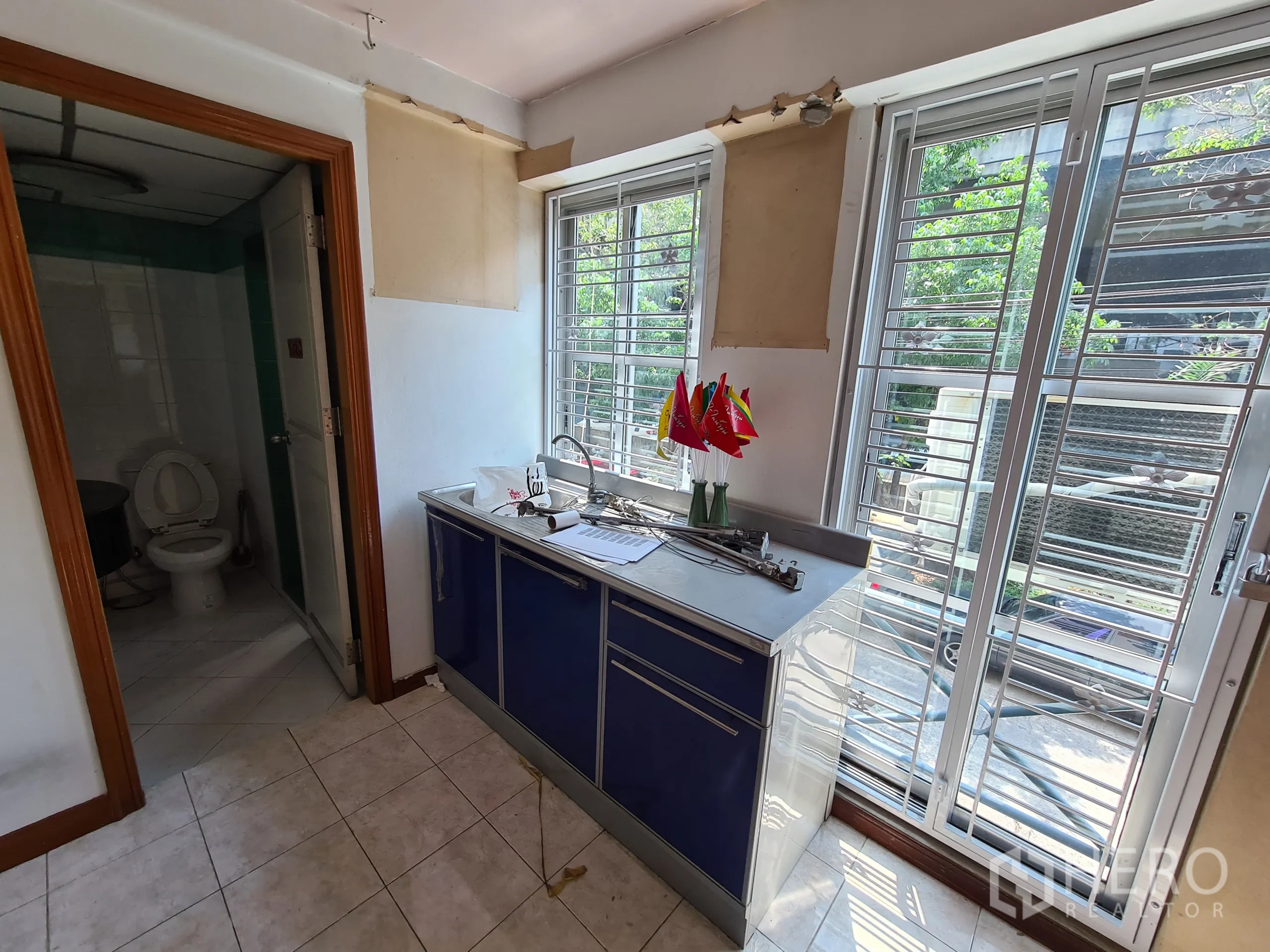 Shophouse for rent or sale in Sathon, Bangkok - Small pantry with sink next to a bathroom and tall windows fitted with metal grilles.