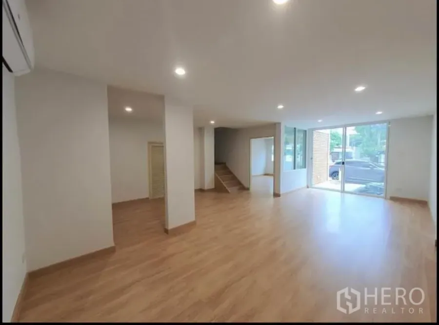 联排别墅 出租在Phaya Thai, Bangkok - 一层采光明亮的开放式空间，木地板、筒灯与推拉玻璃门。
