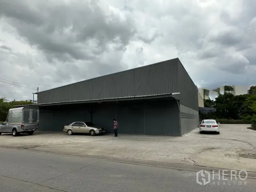 Warehouse for rent in Thanyaburi, Pathum Thani - Front exterior of a gray metal warehouse with wide concrete forecourt, roadside access and roller shutter doors.